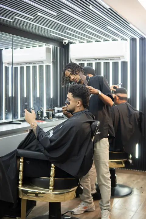 Dos barberos atendiendo a un cliente en una silla dorada